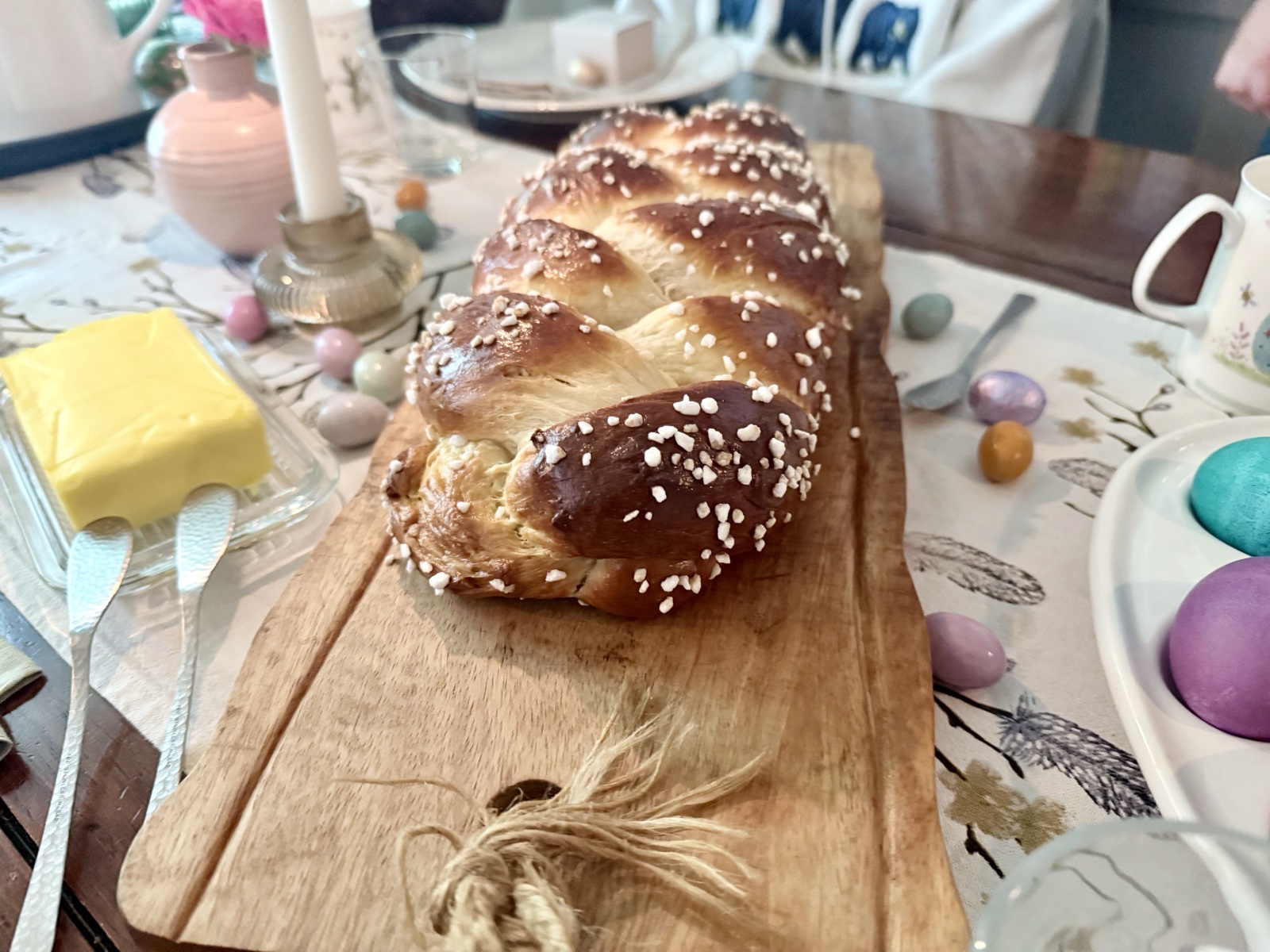 Golden braided Hefezopf with pearl sugar on a wooden board, surrounded by Easter eggs and candles