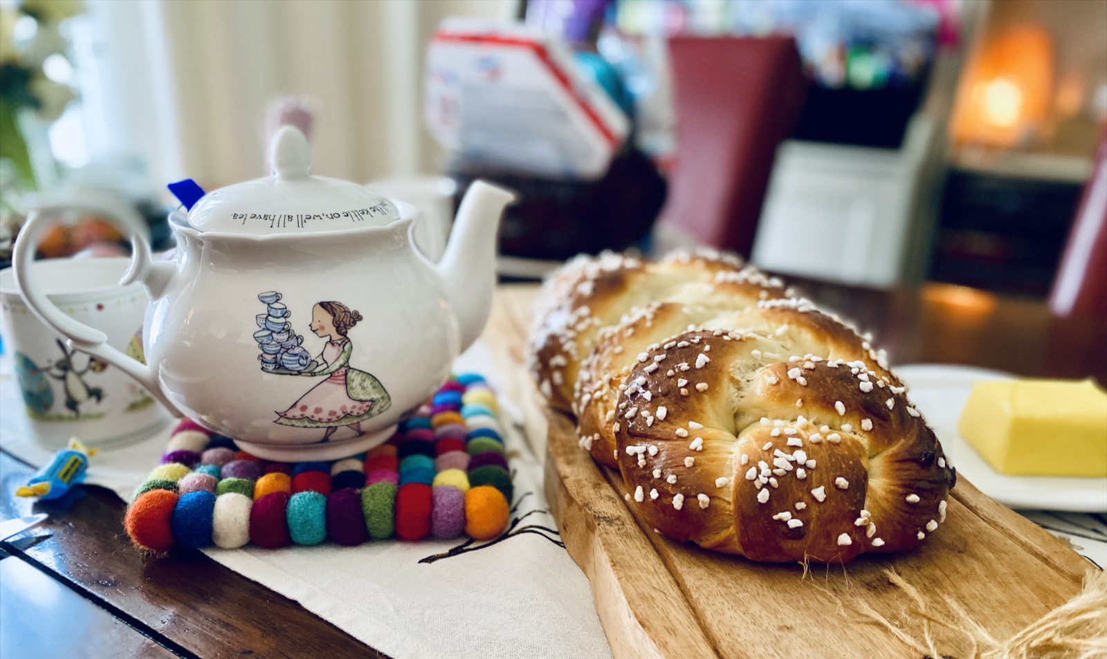 Round braided Hefezopf with pearl sugar on a wooden board next to a teapot and butter