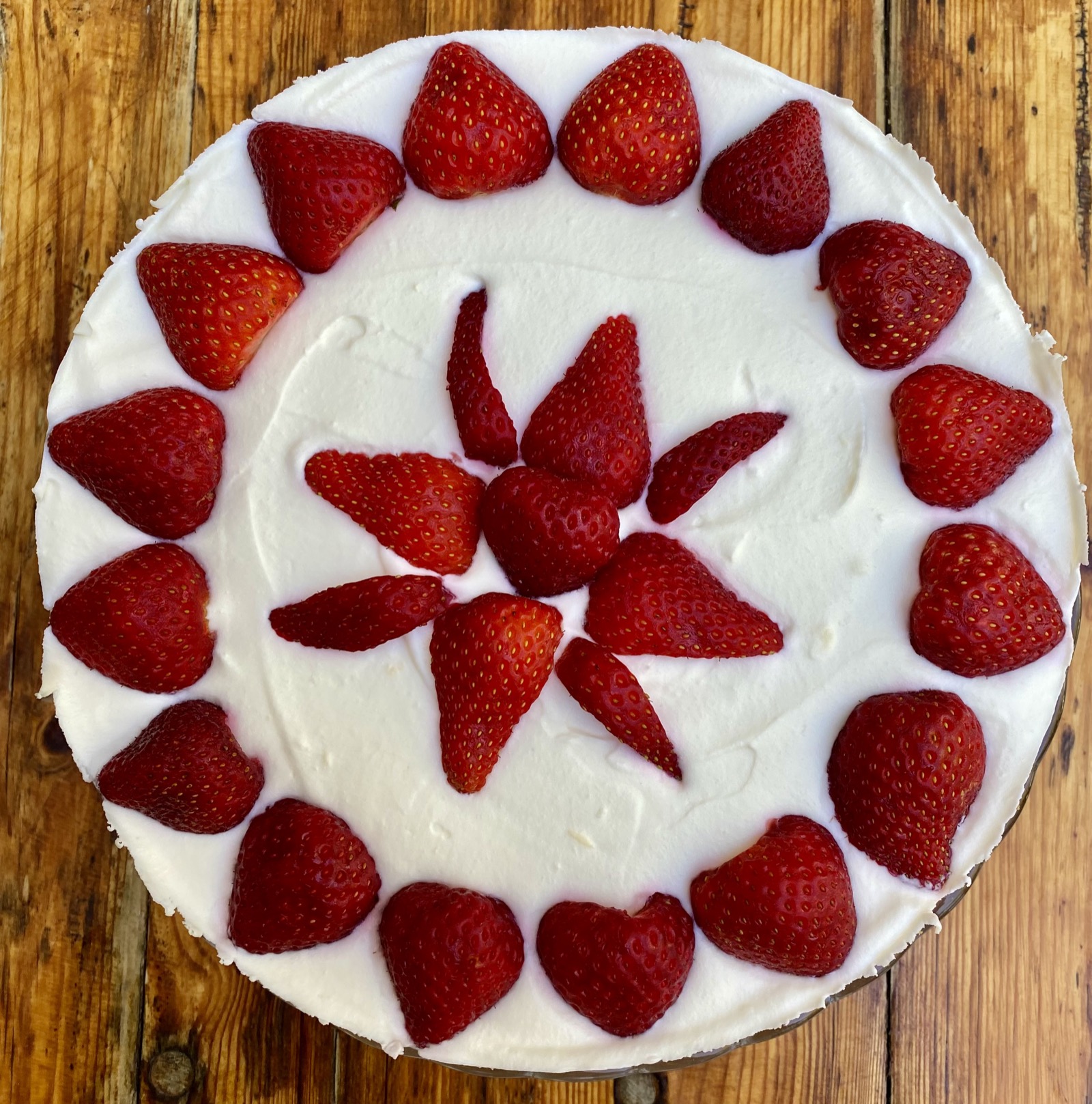 Strawberry cream cake seen from above with fresh strawberries arranged in a circle on white quark cream