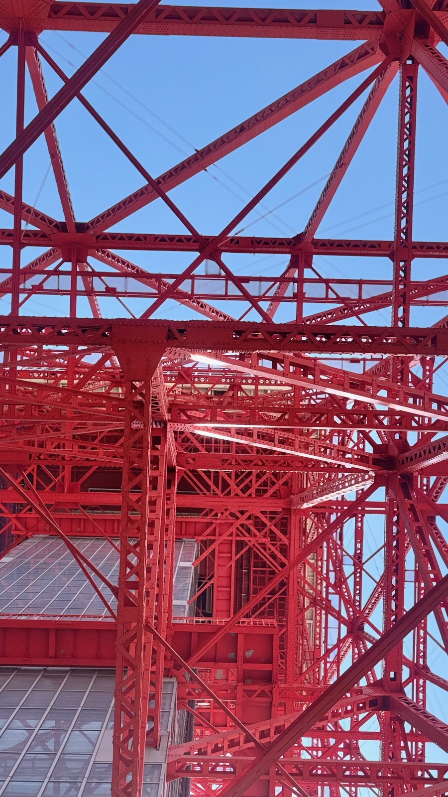 Looking up through Tokyo Tower's iconic international orange steel lattice against a blue sky